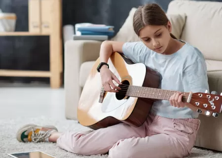 Niña tocando la guitarra en su habitación.